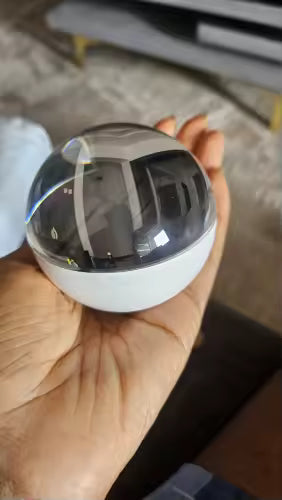 A small spherical smart home device with a glossy black reflective dome and a white base, held in a person's hand.